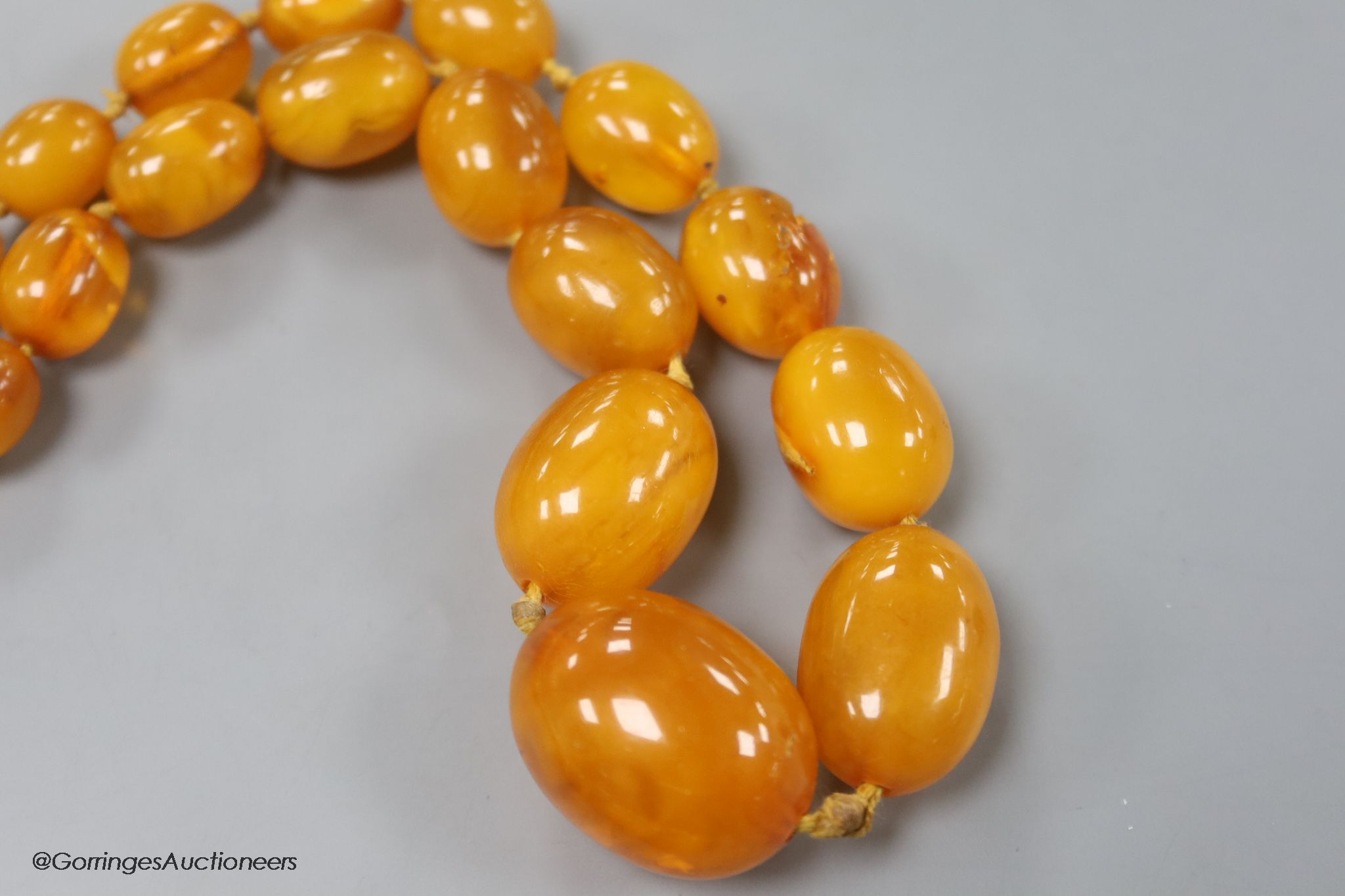 Two single strand graduated oval amber bead necklaces, 71cm, 61 grams & 89cm, 68 grams (beads missing from larger necklace)